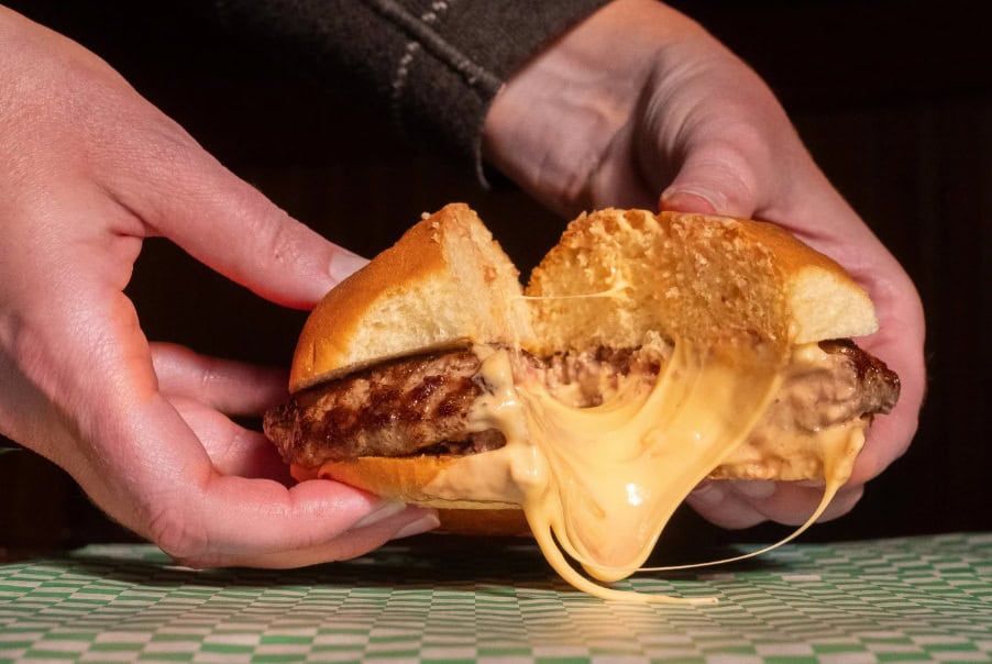 Cheeseburger cut in half with American cheese pouring out of it.