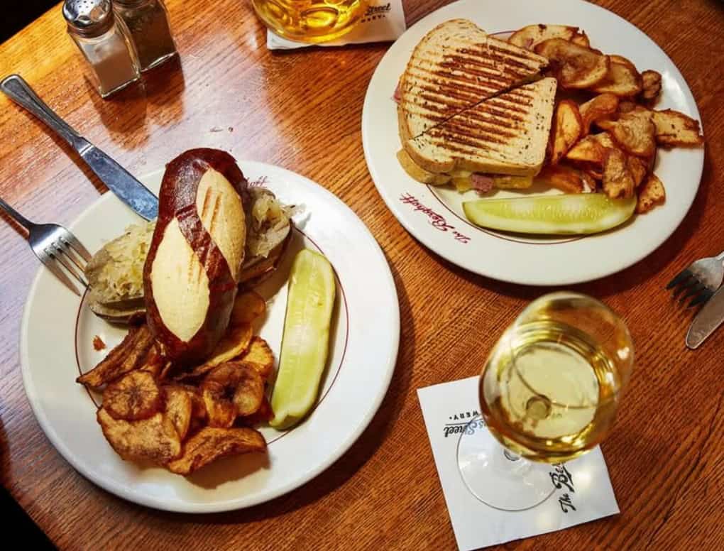 Two plates with food from The Berghoff with a glass of white wine