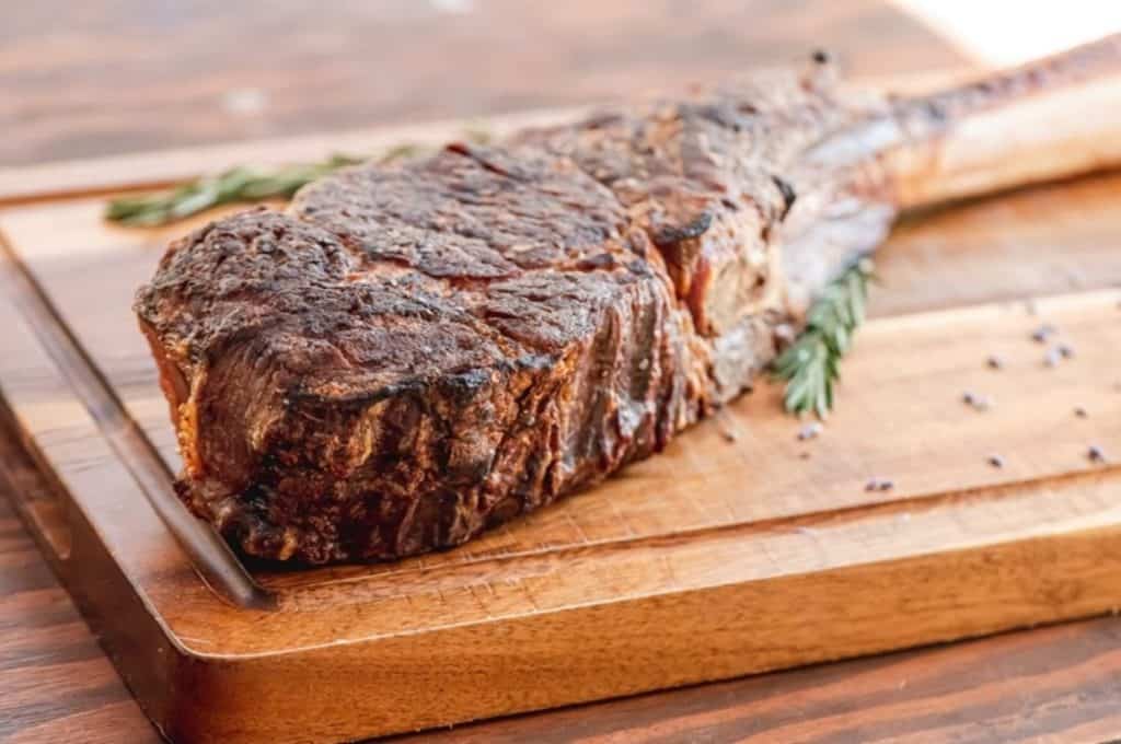 Steak from Gene & Georgetti placed on a wooded cutting board with herbs 