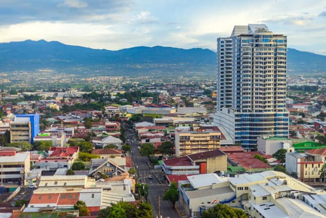 City in costa rica with a high rise apartment and the mountains in the background