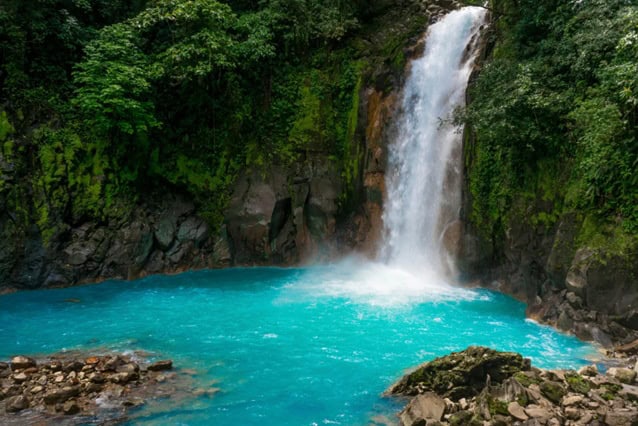 Waterfall in costa rica with the water flowing into a bright blue pool.